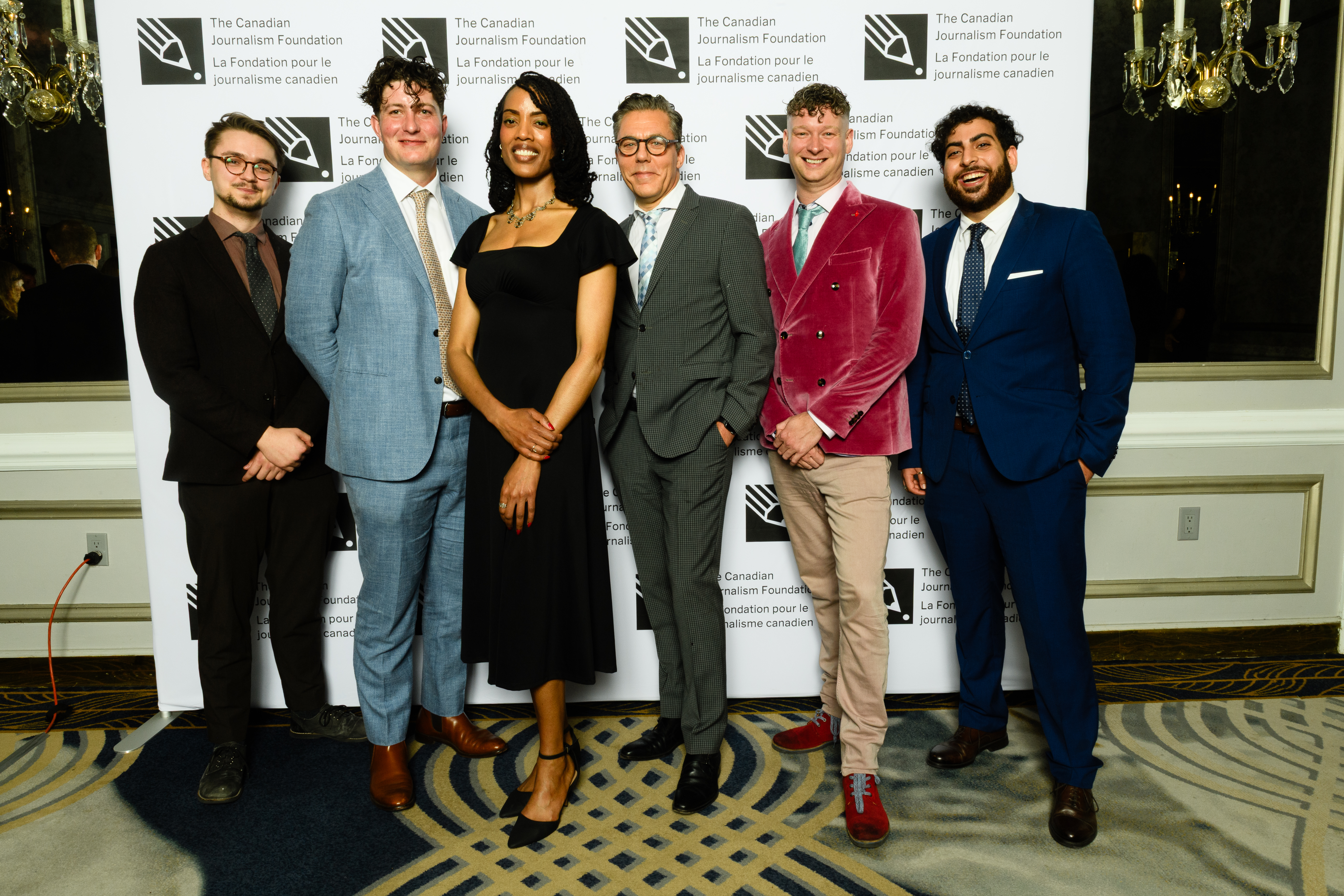 The image depicts a group of six individuals, five men and one woman, posing together in formal attire, likely at an award...